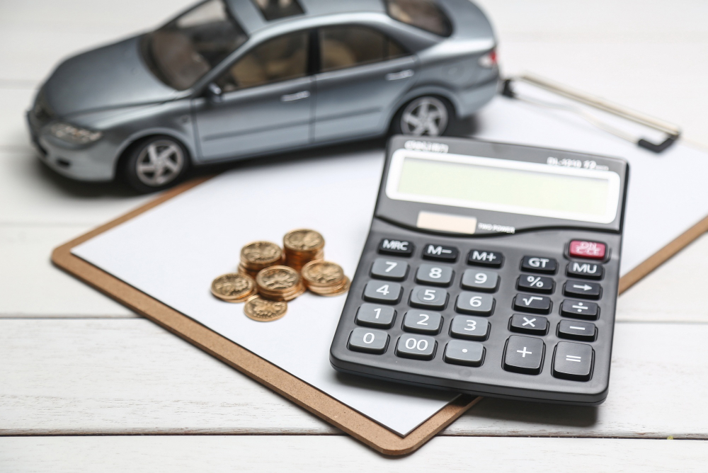 Carro de brinquedo, uma calculadora e moedas sobre uma prancheta representando o crédito automotivo.